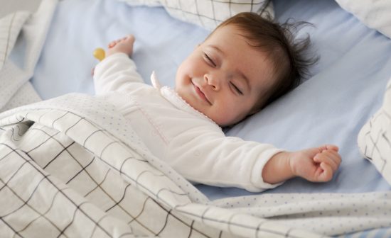 Smiling baby girl lying on a bed sleeping on blue sheets