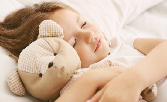 Adorable little girl sleeping with teddy bear in bed