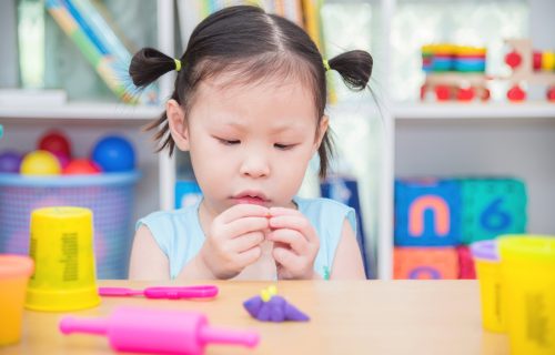 Little asian girl playing with dough on table