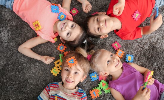 Cute little children playing with colorful figures while lying on carpet at home