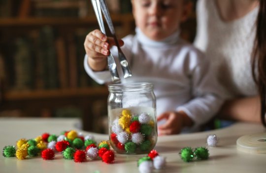 child boy Toddler puts colorful soft balls of toys in a jar, the development of fine motor skills. Previously, the development of the child at home in the real interior.