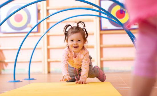 Baby girl crawling on mat in gym class. Lifestyle concept of children activity.