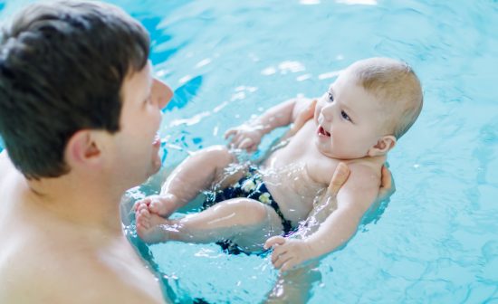 Happy middle-aged father swimming with cute adorable baby in swimming pool. Smiling dad and little child, newborn girl having fun together. Active family spending leisure and time in spa hotel.