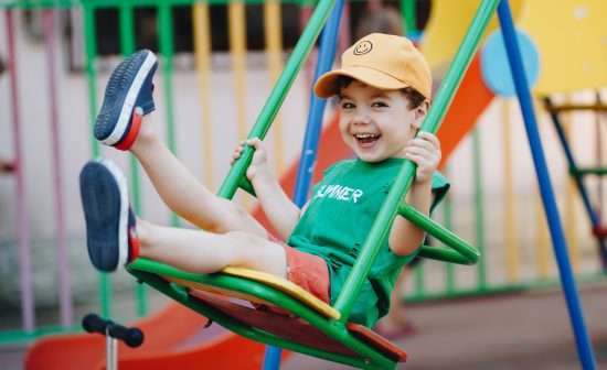 beautiful little boy spinning on a summer swing with space for text.