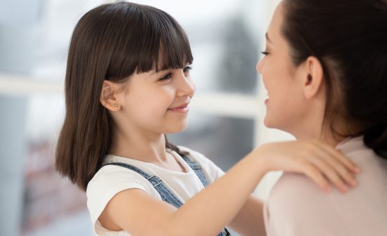 Happy loving mom and cute adorable daughter look at each other. Smiling little girl embracing mum at home in mother day, enjoying free time together. Adoption concept