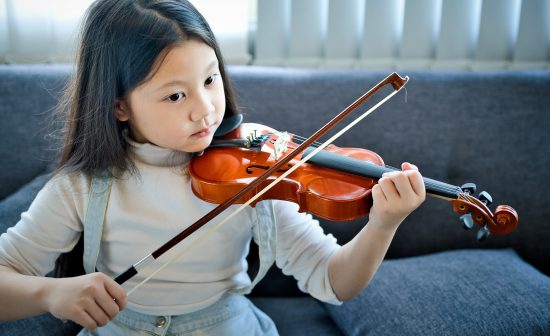 Asian kid learning and practising  to play violin at home