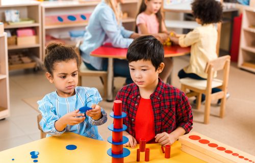 Selective focus of kids folding board game with teacher and children at background in montessori school