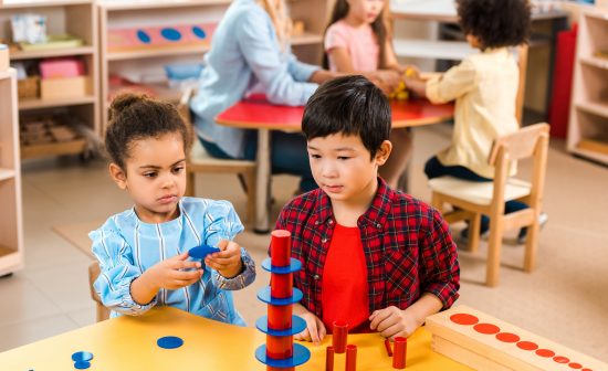 Selective focus of kids folding board game with teacher and children at background in montessori school