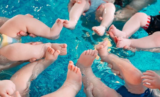 A group of mothers with their young children in a children's swimming class with a coach