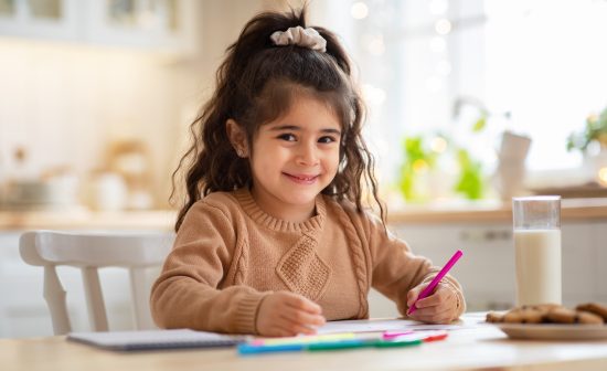 Children Development Activities. Cute Little Preschool Girl Drawing In Kitchen At Home, Adorable Female Child Sitting At Table With Pencil In Hand And Smiling At Camera, Copy Space