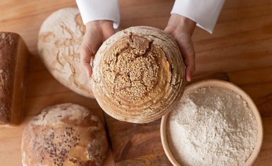 From above anonymous kid holding fresh loaf of bread over table with flour in bakery