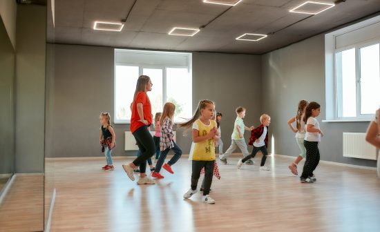 Group of little boys and girls dancing while having choreography class in the dance studio. Female dance teacher and children. Contemp dance. Hip hop. Kids and sport. Full length