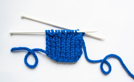 top view of blue wool yarn and knitting needles on white background