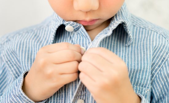 Child Development concept: Close up of a little kindergarten boy's hands learning to get dressed, buttoning his striped blue shirt. Montessori practical life skills - Care of self, Early Education.